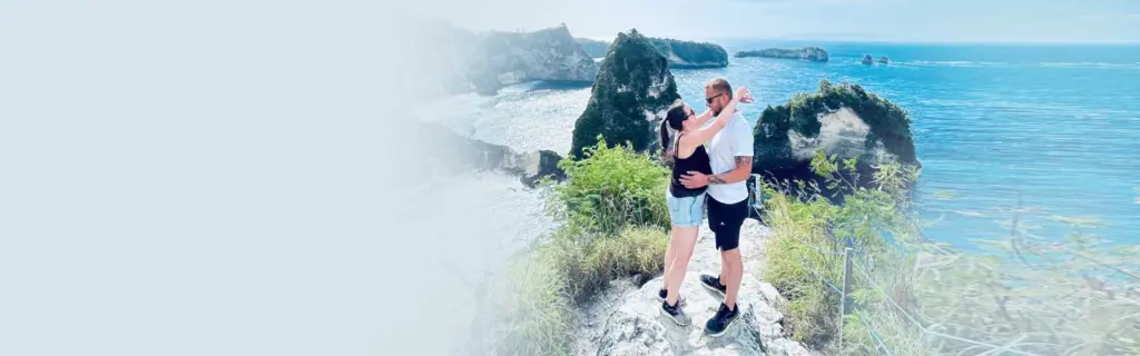 A romantic couple embracing on a cliff with a spectacular ocean view during their Nusa Penida travel.